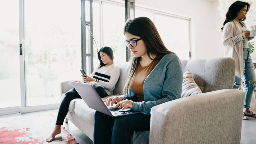 graduate application cover letter Two young women sat on a sofa, one looking at her phone, the other a laptop. A third woman walks behind.
