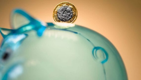 A one pound coin resting on top of a piggy bank