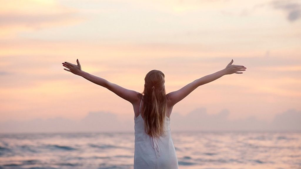 Female raising her arms to the sky in a peaceful setting