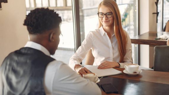 Two people sat having a meeting / interview and drinking coffee