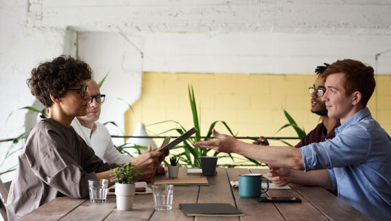 Image of graduates sat around a table with manager working on a project and sharing ideas