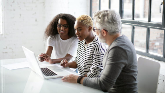 Two graduates smiling showing manager their work on a laptop